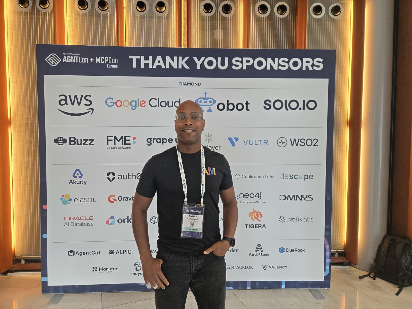 Andre Cobham at the AGNTCon + MCPCon Europe 2026 sponsor wall in Amsterdam